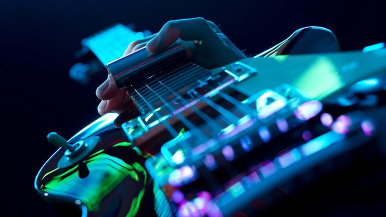 Detalhe da mão de um guitarrista tocando sua guitarra Les Paul com um slide