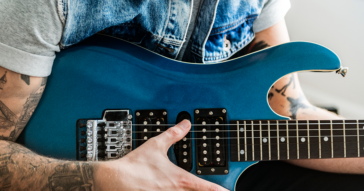 Close em um guitarrista tatuado com uma guitarra azul